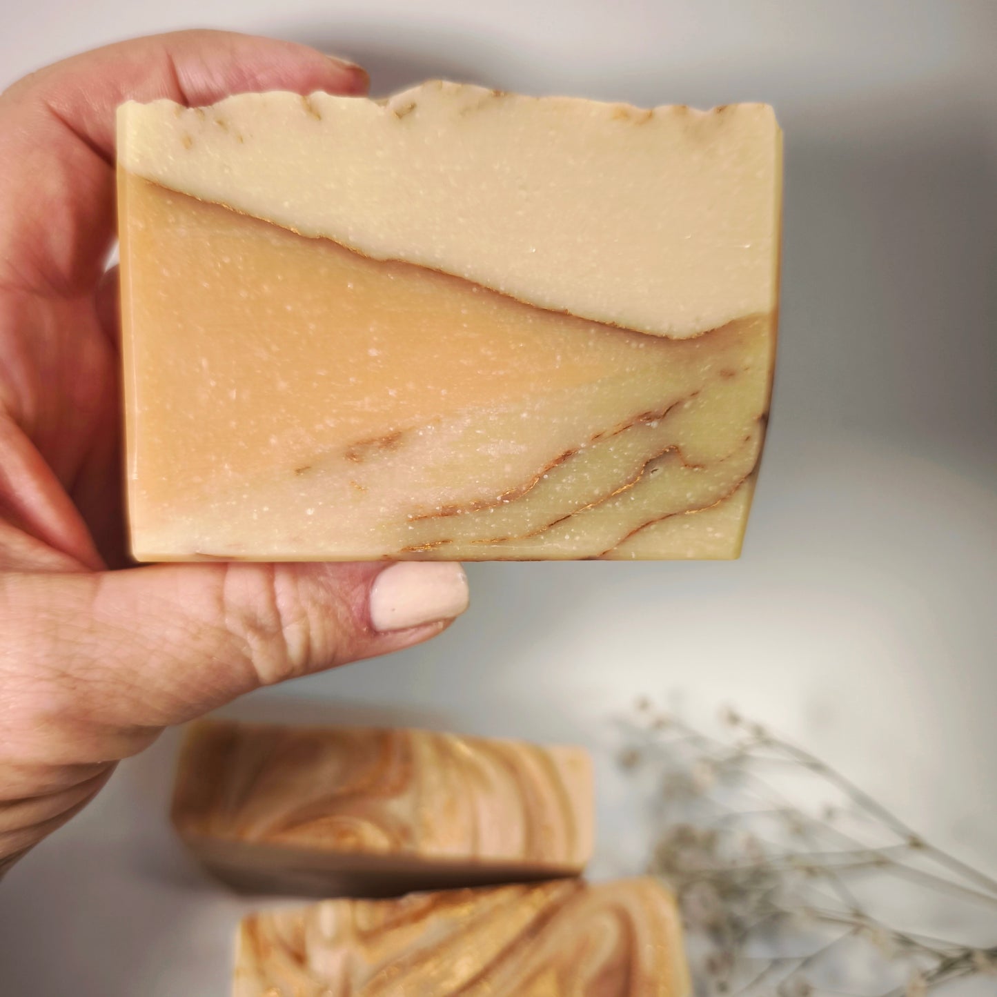 Hand holding a bar of soap with a marble-like pattern on a neutral background