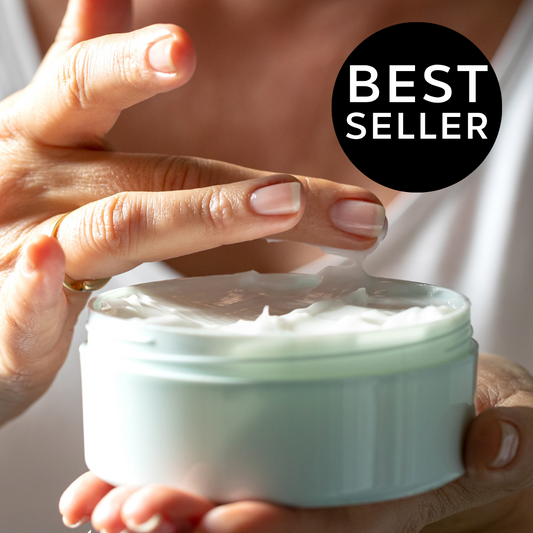 A close-up of a person holding an open round jar of rich body butter, with fingers touching the surface. 