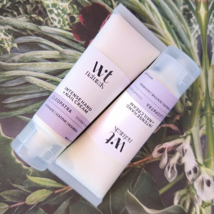 Two Wriggly Tin Naturals Intense hand cream tubes, on a background of green leaves and purple flowers.