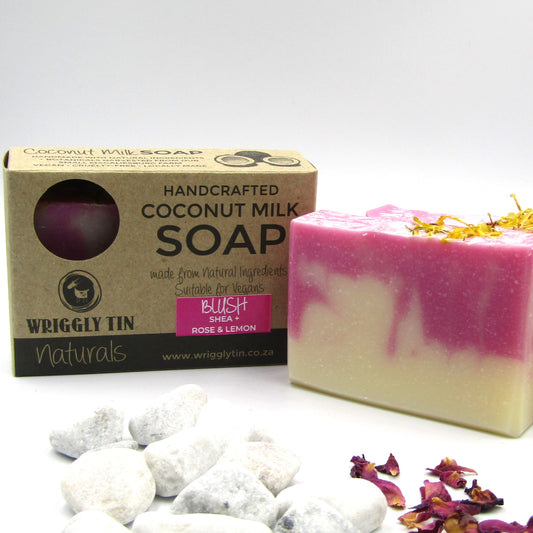 A bar of coconut milk soap with a pink and white swirl design, next to its packaging box, with natural ingredients like shea butter and rose petals mentioned, and a general earthy color theme.